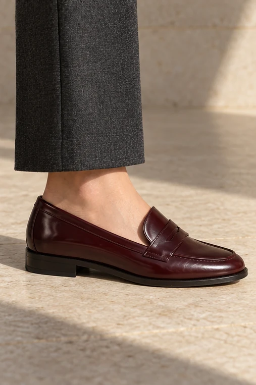Deep oxblood penny loafer beneath charcoal tailored trousers.
