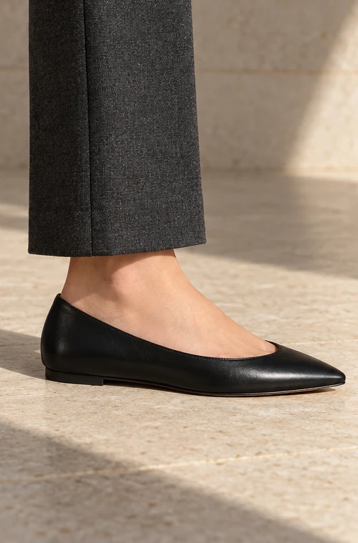 Black pointed flat with a low sole beneath charcoal tailored trousers.
